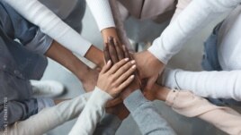 FILE - Business team putting hands together on top of each other. (Prostock-studio via Adobe Stock)