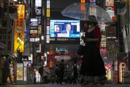 Pedestrians walk past a giant public TV with a live broadcast of a news conference by Japanese Prime Minister Yoshihide Suga after he announced a state of emergency because of rising coronavirus infections Thursday, July 8, 2021, in Tokyo.