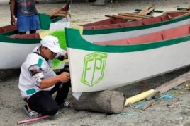 In this April 2, 2019, photo, a member of Islamic Defenders Front paints their group's logo as they help local fishermen to build boats at a fishing village affected by the 2018 tsunami in Palu, Central Sulawesi, Indonesia.