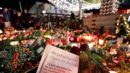 People stay in front of candles close to a Christmas market beside the Kaiser Wilhelm memorial church in Berlin, Germany, Dec. 21, 2016, two days after a truck ran into a crowded Christmas market there, killed several people and injuring dozens.