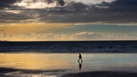 A person walks on Orewa Beach in Auckland, New Zealand, on June 5, 2021. New Zealand has recorded its warmest June since recordkeeping began, as ski fields struggle to open and experts predict shorter southern winters in the future. (Brett Phibbs/New Zealand Herald via AP)