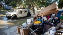 A military vehicle passes flood-damaged belongings piled on a homeowners' front lawn in the aftermath of Hurricane Harvey at the Canyon Gate community in Katy, Texas, Sept. 7, 2017.