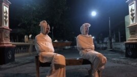 Volunteers Deri Setyawan, 25, and Septian Febriyanto, 26, sit on a bench as they play the role of 'pocong', or known as 'shroud ghost', to make people stay at home amid the spread of coronavirus disease (COVID-19), outside the gate of Kepuh village in Suk