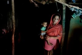 In this Aug. 27, 2018, photo, Rohingya refugee woman Minara Begum, mother of Rahima Akter, holds her youngest daughter Arohi Zannat inside the family hut in Kutupalong refugee camp, Bangladesh.