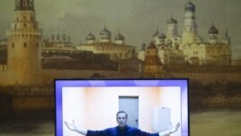 Russian opposition leader Alexei Navalny appears on a TV screen during a live session with the court during a hearing of his appeal in a court in Moscow, Russia, Thursday, Jan. 28, 2021, with an image of the Moscow Kremlin in the background. 