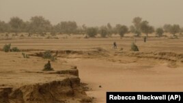People walk past a dry seasonal riverbed in the Matam region of northeastern Senegal.