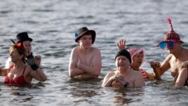 People with hats and caps attend the annual New Year's swimming of the winter swimming club Berliner Seehunde (Berlin Seals) at Oranke Lake in Berlin, Monday, Jan. 1, 2018. (AP Photo/Markus Schreiber)