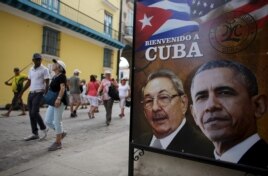 Tourists pass by images of U.S. President Barack Obama and Cuban President